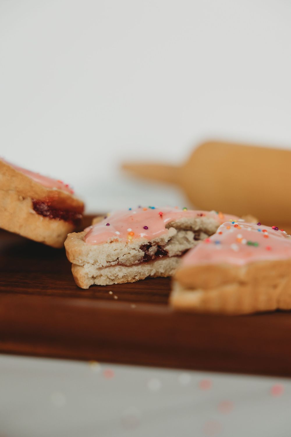 Close-up view of split sandwich cookies with pink frosting and berry filling on a wooden board.
