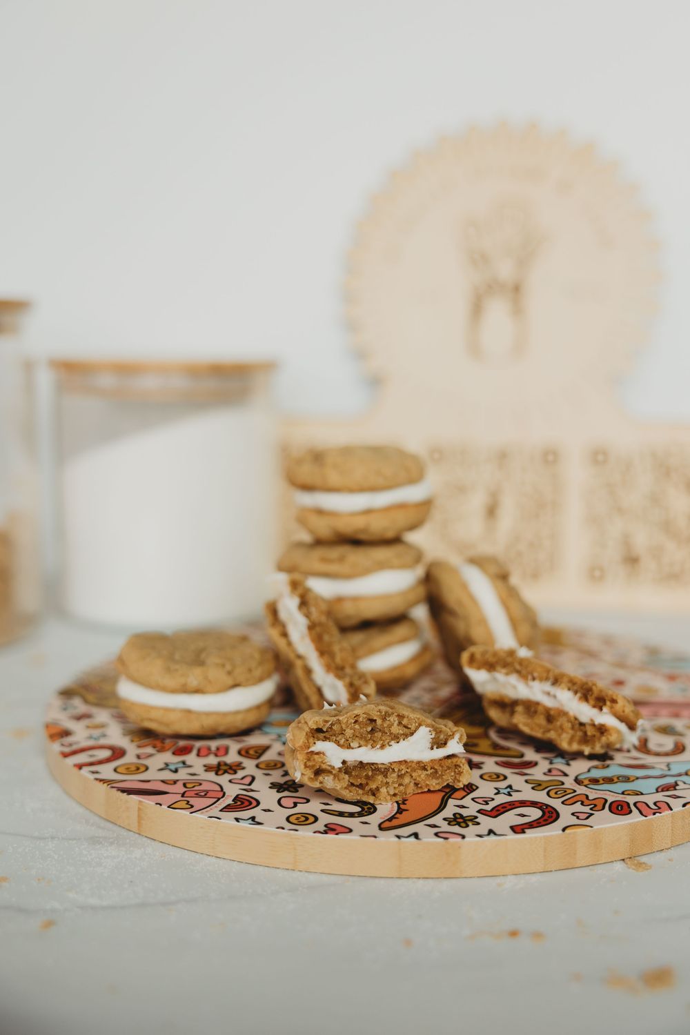 Homemade sandwich cookies with cream filling arranged on a decorative wooden serving board with milk.