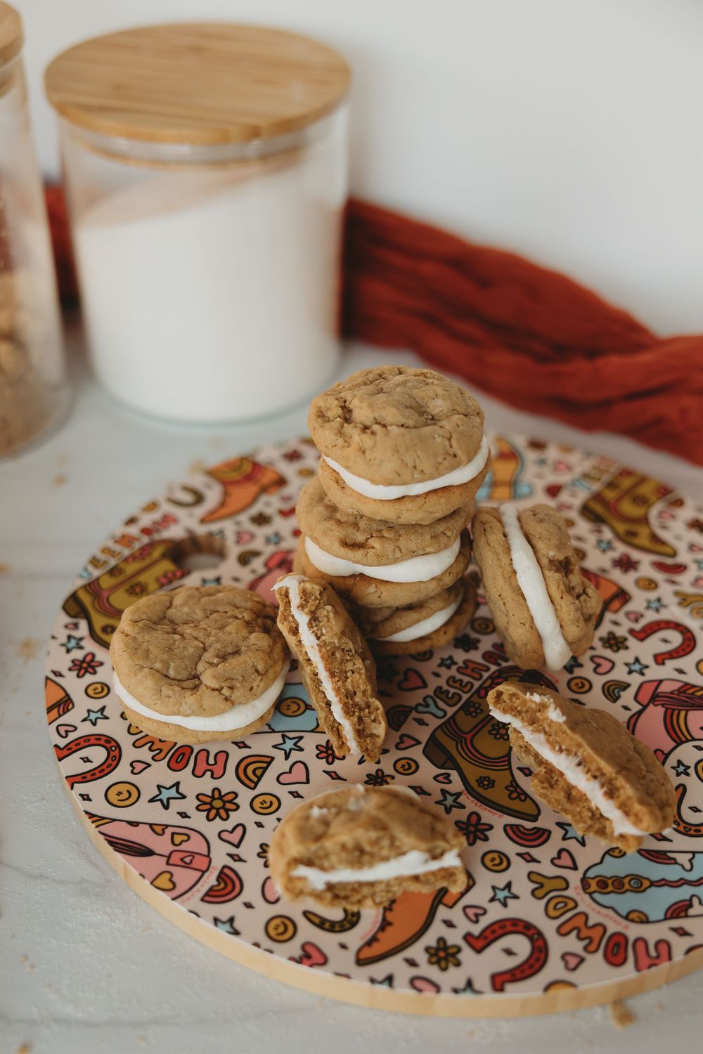 Stacked cream-filled sandwich cookies displayed on a colorful patterned plate with a glass of milk nearby.
