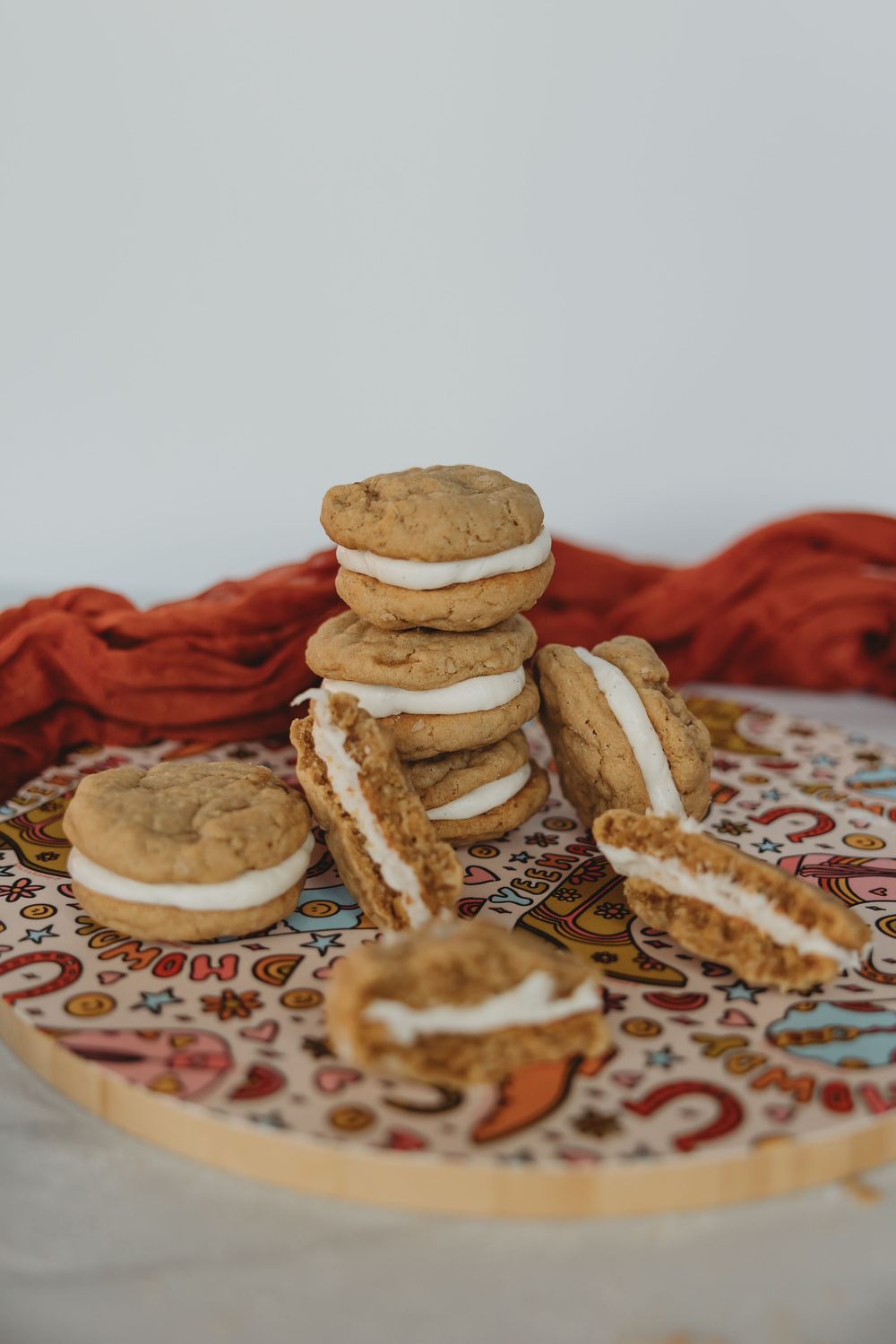 Homemade sandwich cookies with cream filling arranged on a decorative paisley patterned surface next to a red cloth.