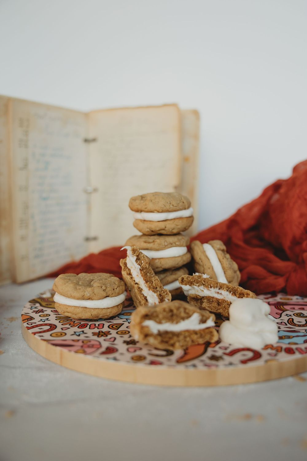 Sandwich cookies with cream filling arranged on a decorative patterned surface with a red cloth.