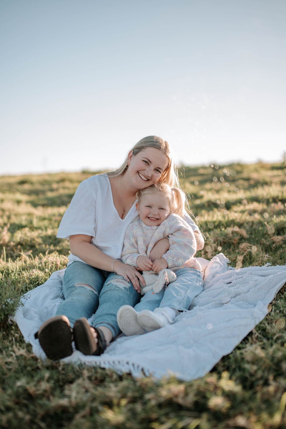 Parent and child enjoying a tender moment together while sitting on a blanket in a sunny field at sunset.