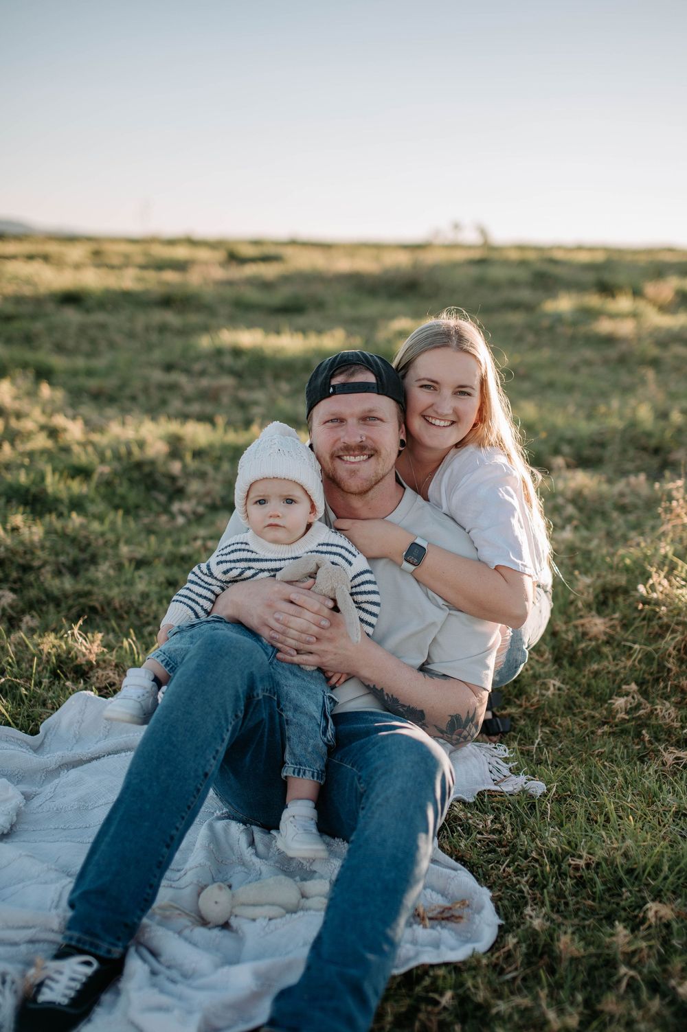 Young family relaxing together on picnic blanket in grassy field during golden hour sunset.