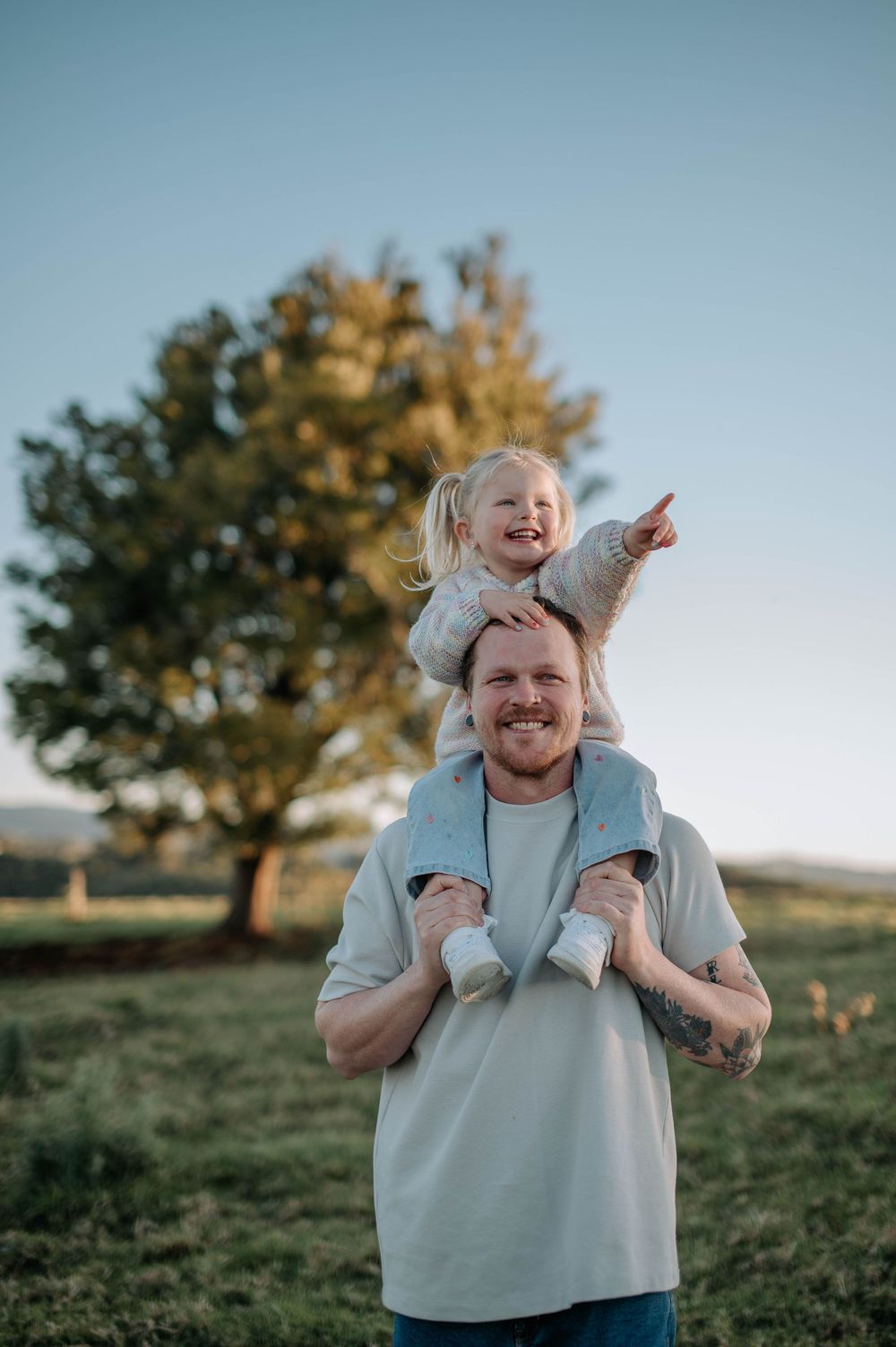 A joyful moment captured outdoors with someone sitting on shoulders pointing into distance during golden hour.
