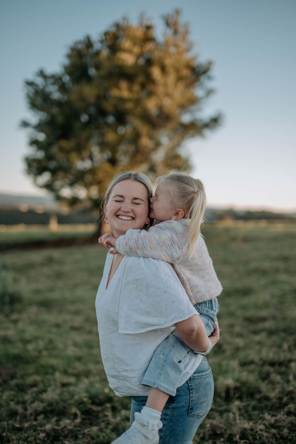 Sweet outdoor moment features a tender embrace between two people in a grassy field at golden hour.