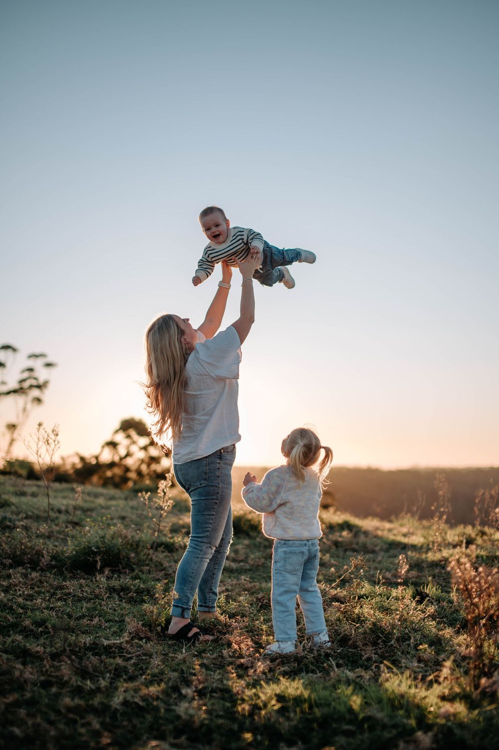 A family plays together in a grassy field at sunset as golden light illuminates joyful moments of connection and laughter.