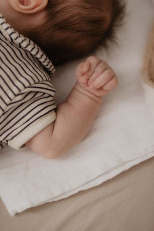 Peaceful close-up of small hands against striped fabric and white bedding.
