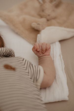 Delicate close-up of baby's hand resting on white fabric against beige background.