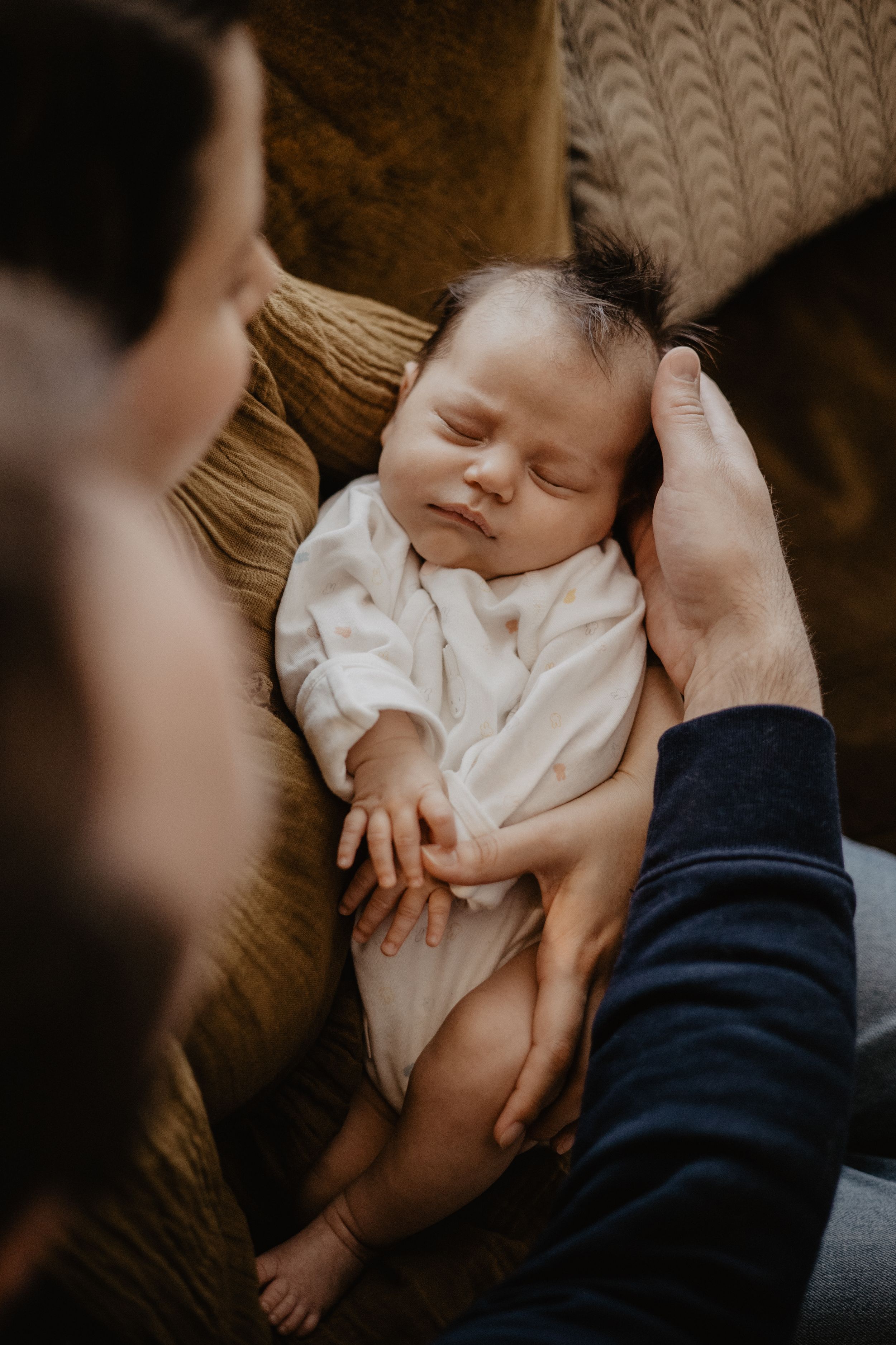 Newborn baby in white clothing sleeping peacefully on textured brown fabric.