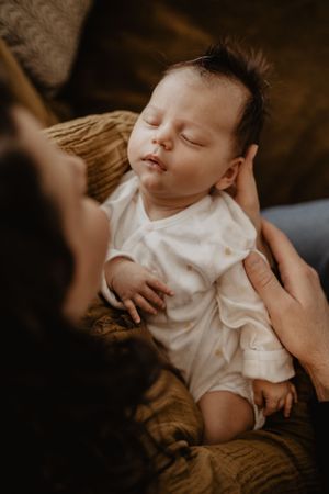 A peaceful sleeping baby in a white onesie rests on brown fabric.