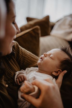 Baby naps peacefully on dark colored blanket in white clothing.