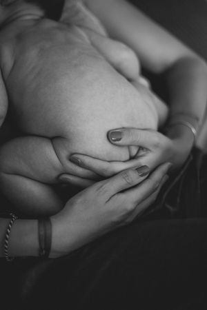 Close-up black and white photo of hands gently cradling a baby in soft natural light.