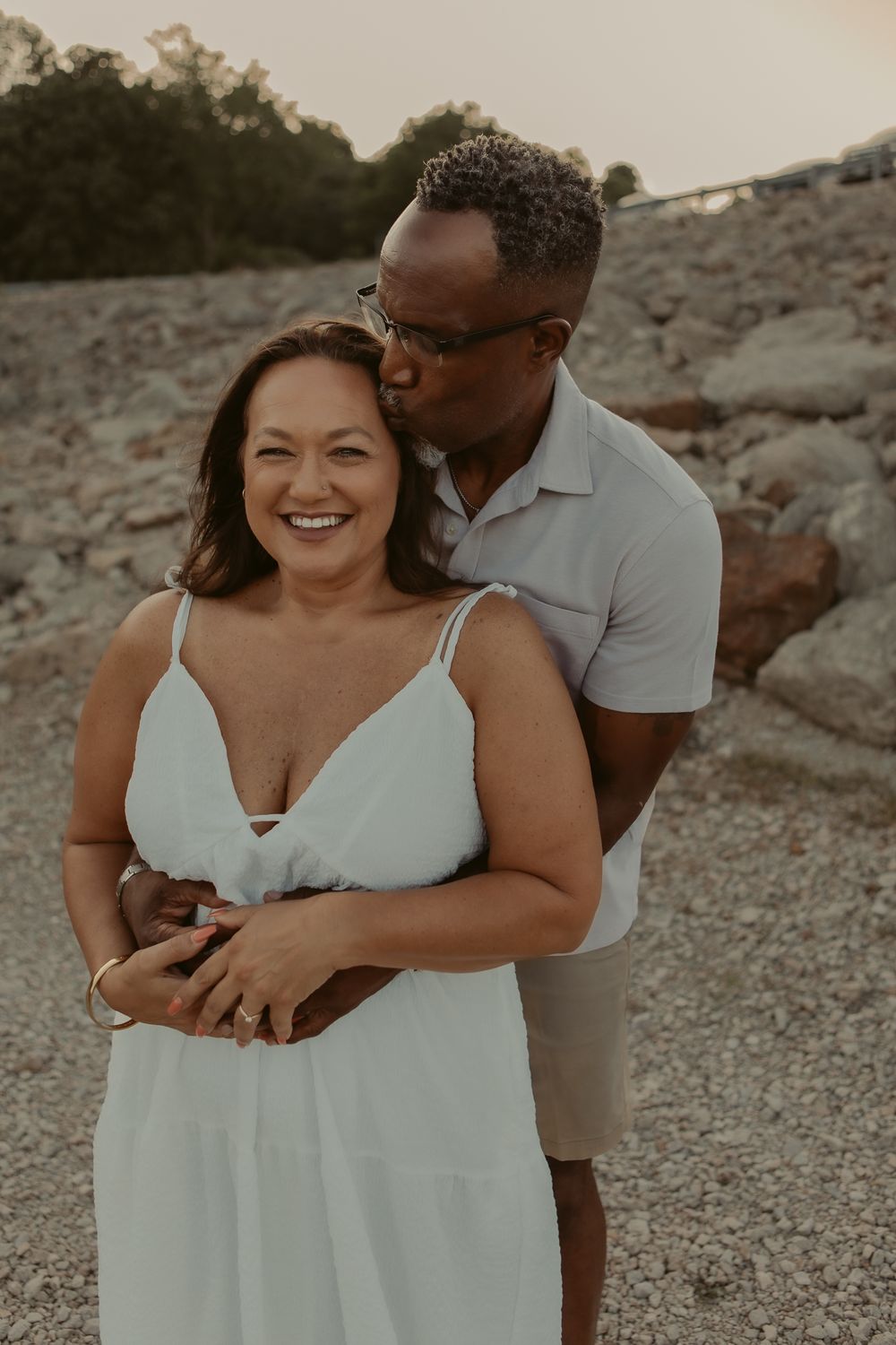Intimate couple photoshoot on a rocky beach at sunset showing playful embraces and casual romantic moments.