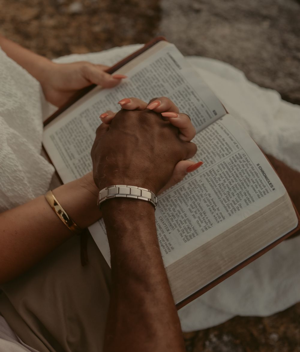 Close-up shot of hands resting on an open book against a moody dark background.