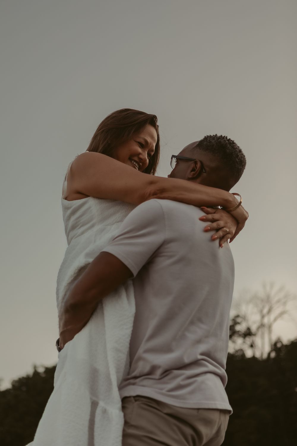 A gentle embrace between two people wearing light colored clothing captured in a series of connected soft dusk photos.