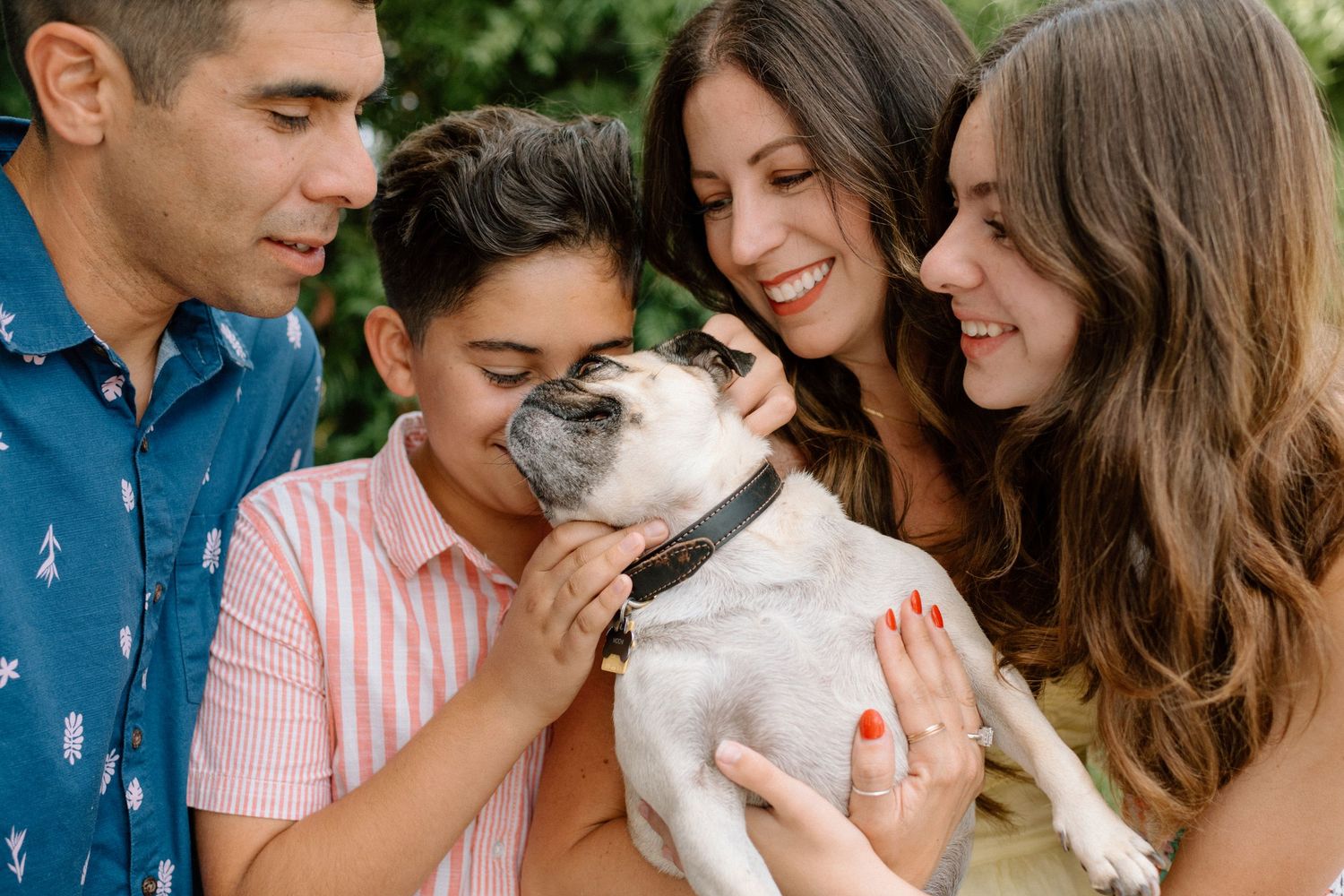 A happy family shares a joyful moment outdoors with their white French bulldog pet.