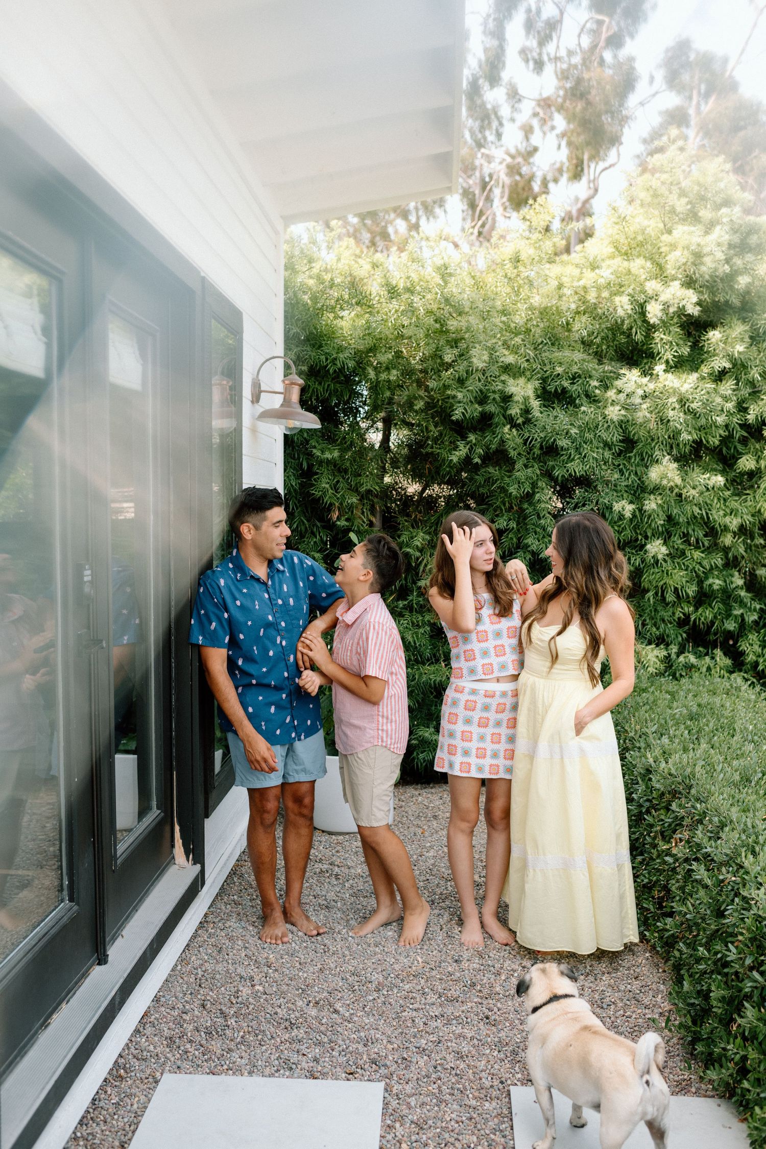 Group of friends enjoying a casual outdoor gathering on a porch with a dog while surrounded by lush greenery.