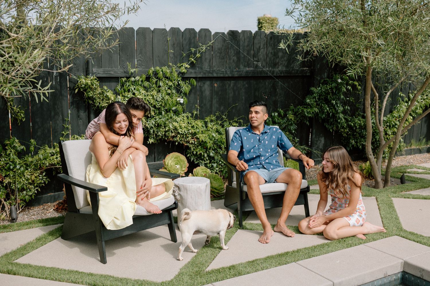 Group of friends relaxing and lounging together on outdoor cushions in a sunny garden setting.
