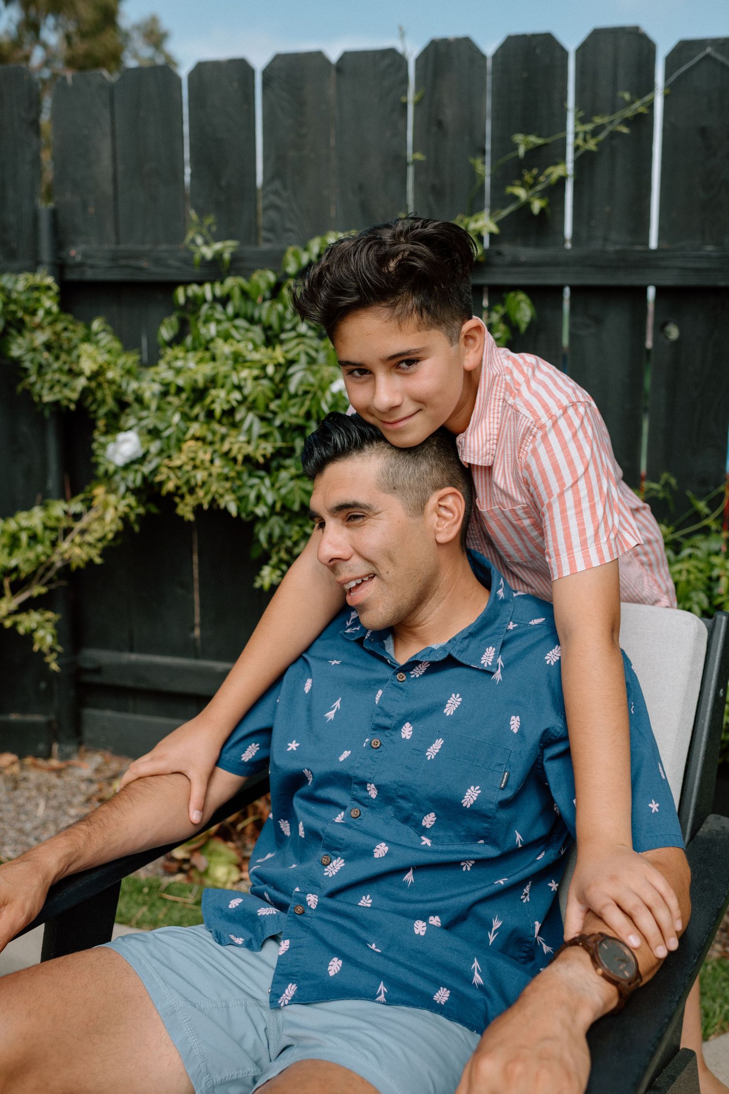 A joyful outdoor portrait showing a playful bonding moment against a dark wooden fence on a sunny day.