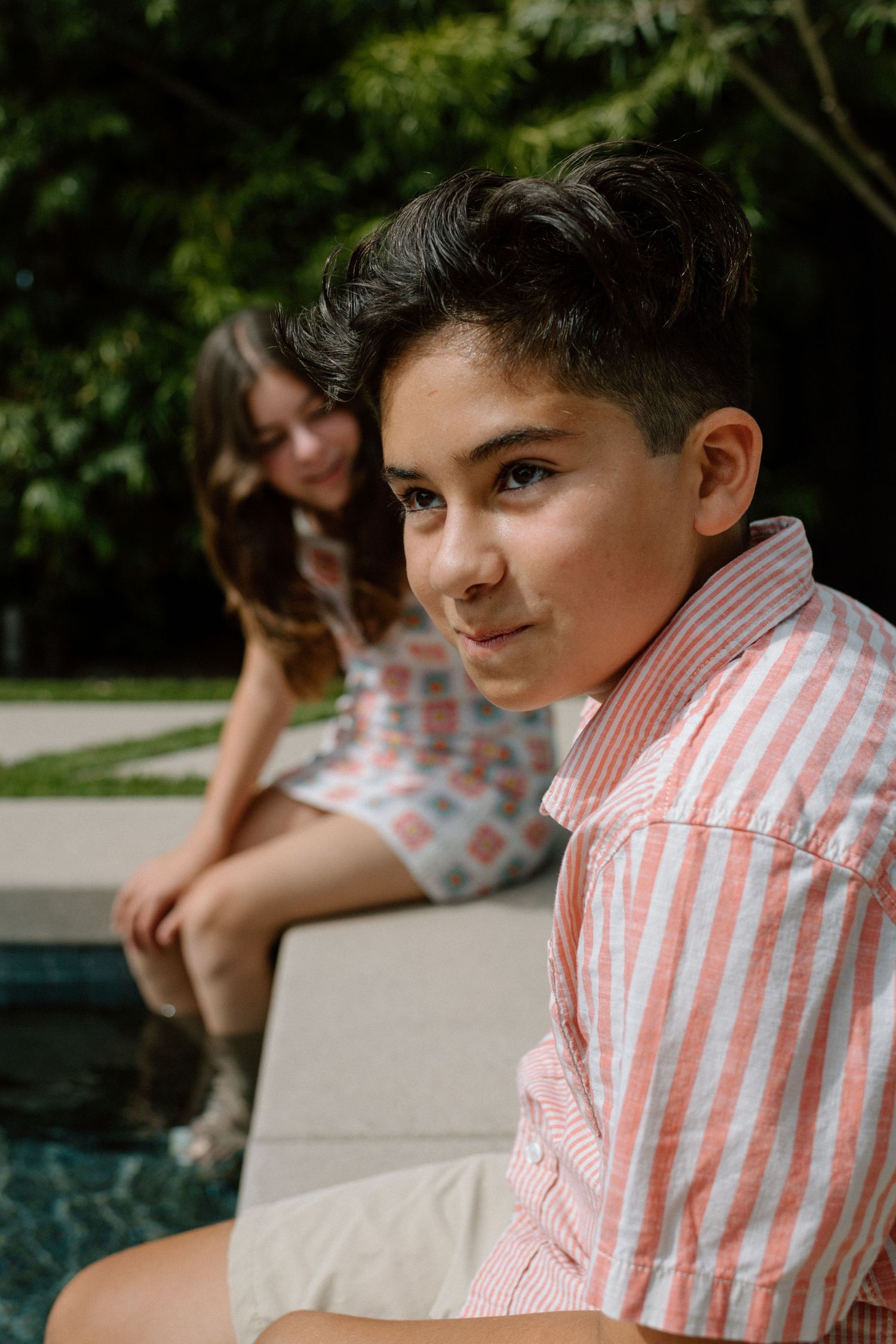 Three siblings sit together by a pool on a sunny day wearing red and white striped clothing.