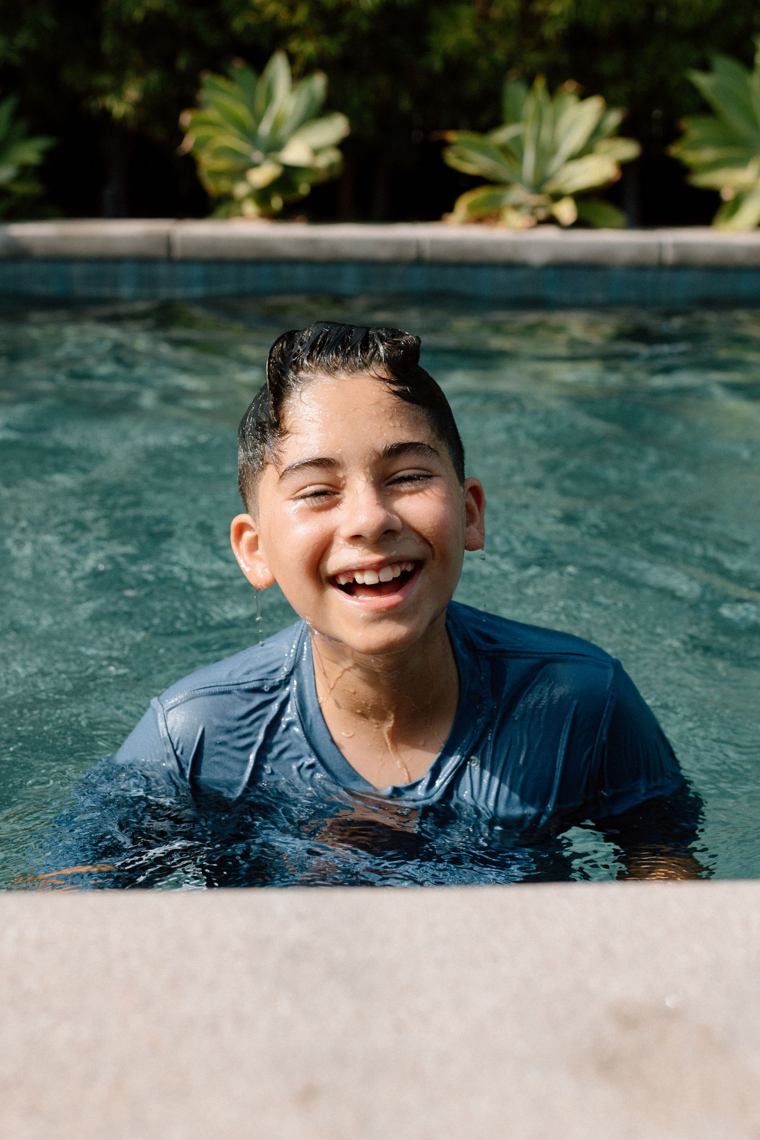 Someone enjoys a refreshing swim in a blue pool on a sunny day with plants visible along the edge.