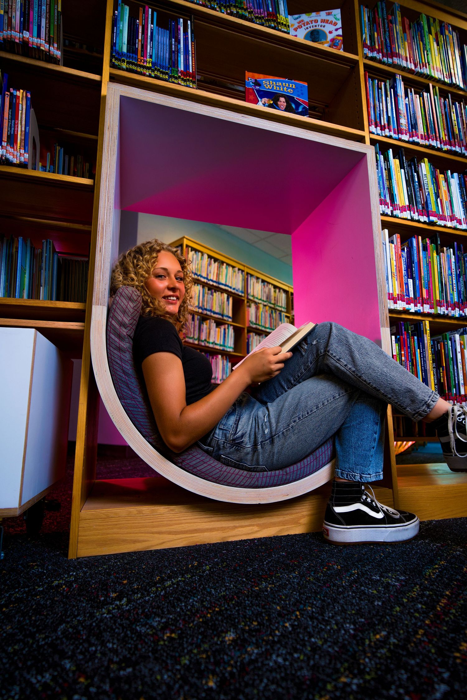 Person relaxing and reading in a cozy library nook with bookshelves in the background.