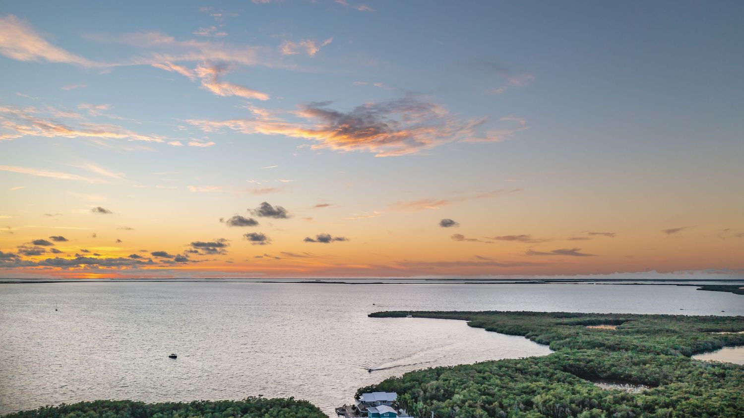 Beautiful sunset sky with orange and pink clouds over water and coastal landscape.
