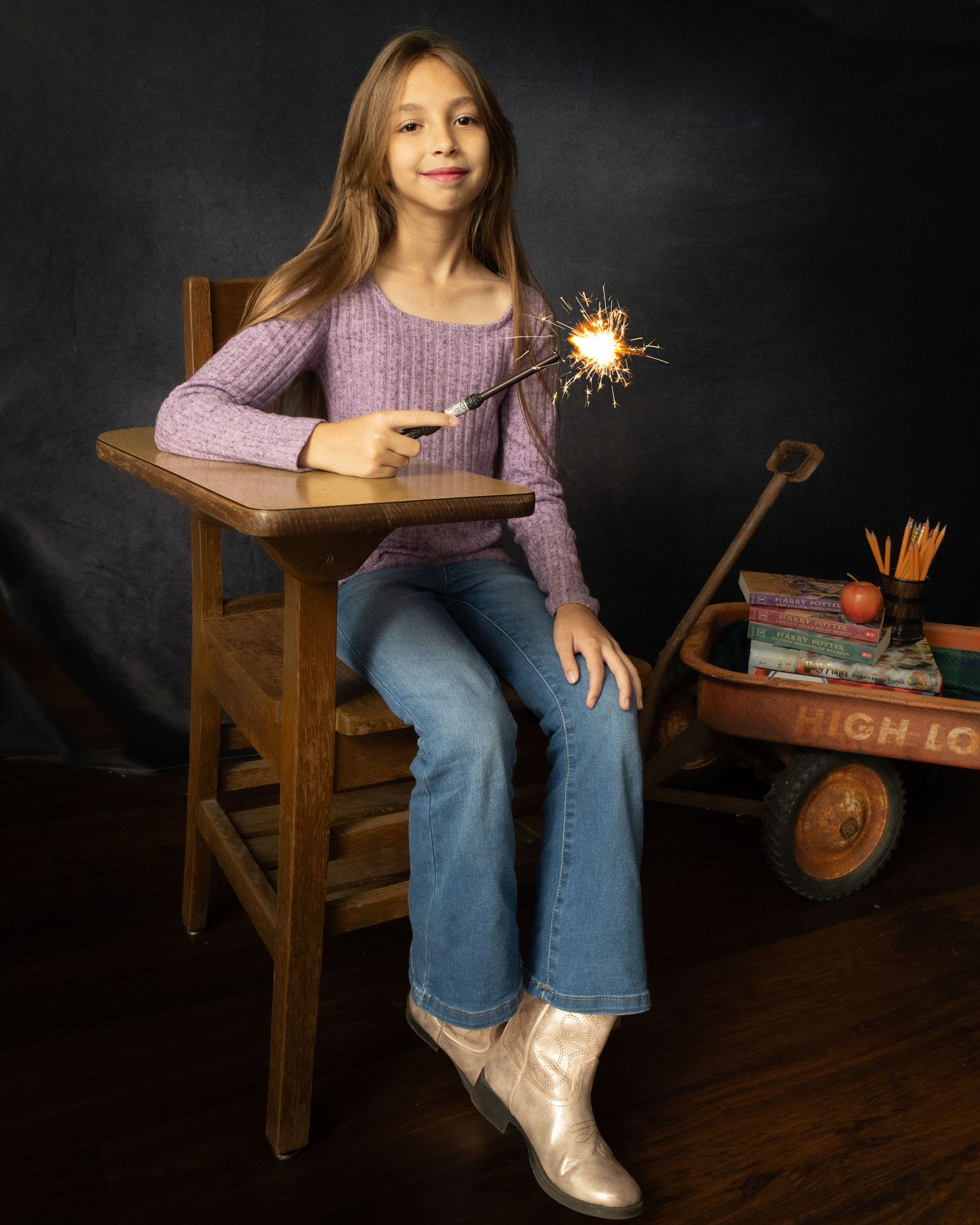 Child in purple sweater sits on wooden bench holding sparkler against dark background, showing joy and wonder.