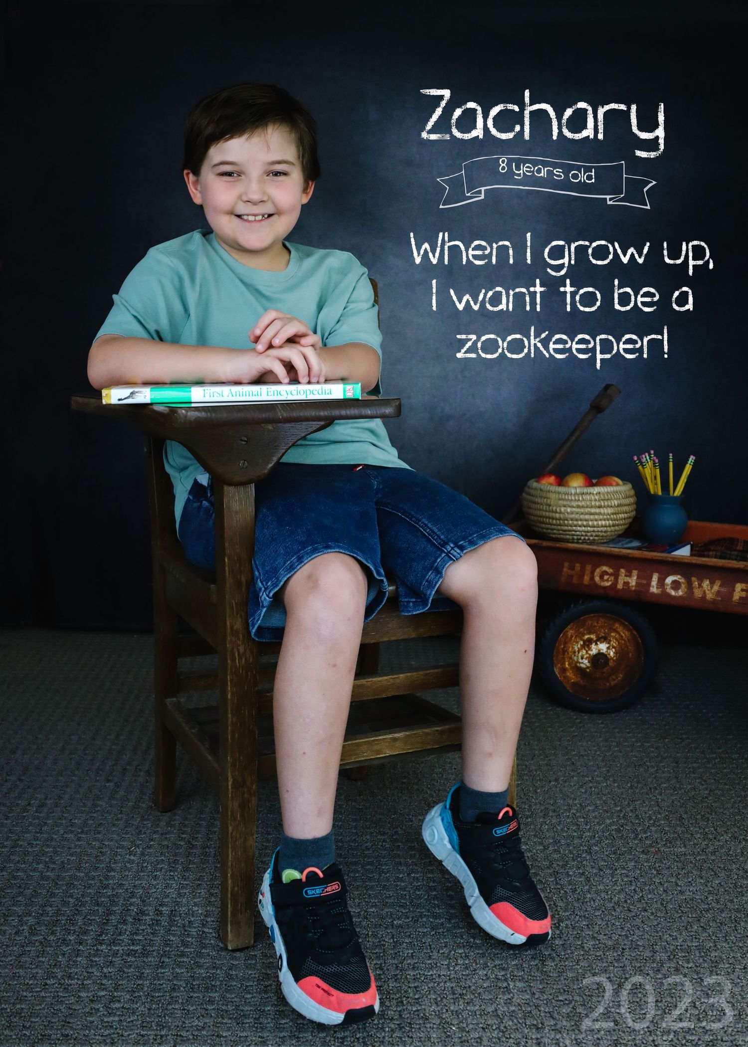 A child sits on a wooden bench in front of a chalkboard showing career aspirations for 2023.