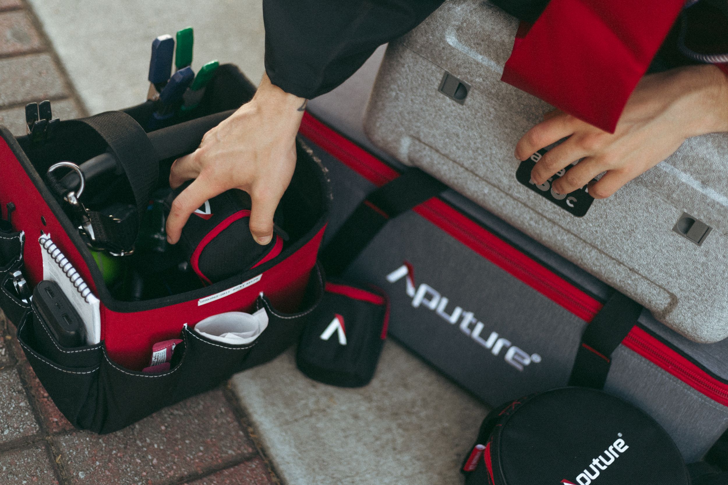 A person packs camera and video equipment into professional black and red Manfrotto equipment bags.