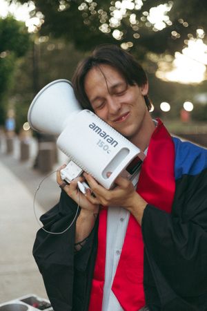 Someone in colorful clothing hugs an Amazon megaphone speaker with eyes closed in a dreamy outdoor setting with bokeh lights.