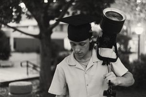 Professional photographer holds heavy telephoto lens and camera on shoulder while shooting outdoors in black and white.