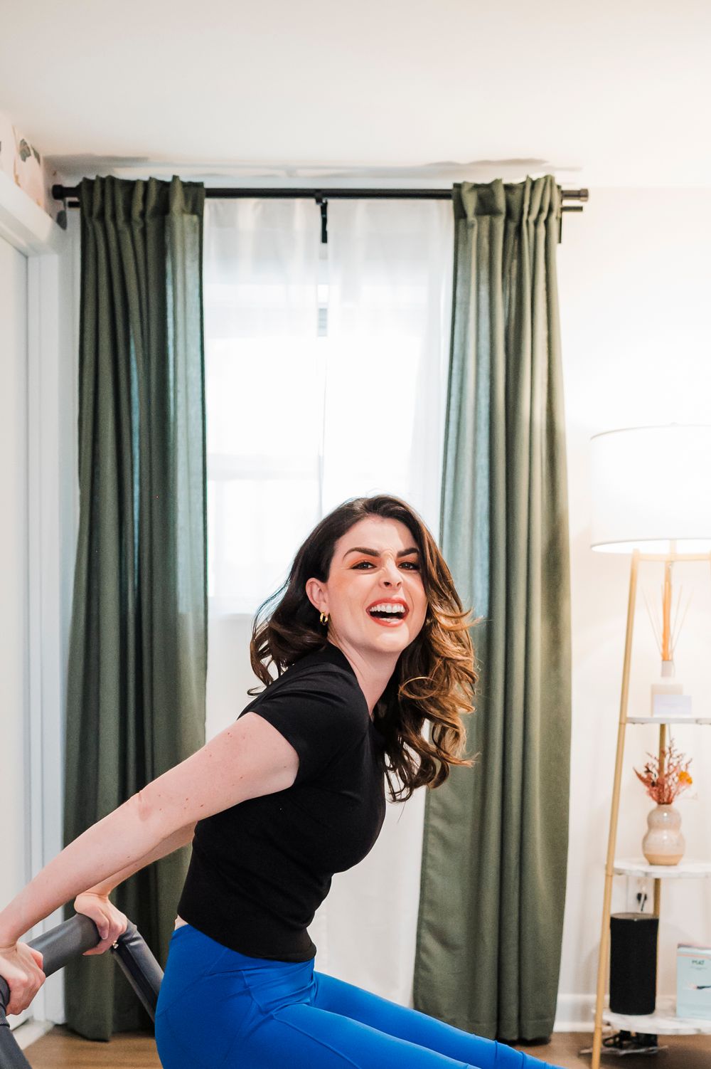 Person performing a dynamic workout movement in a home exercise space with green curtains.