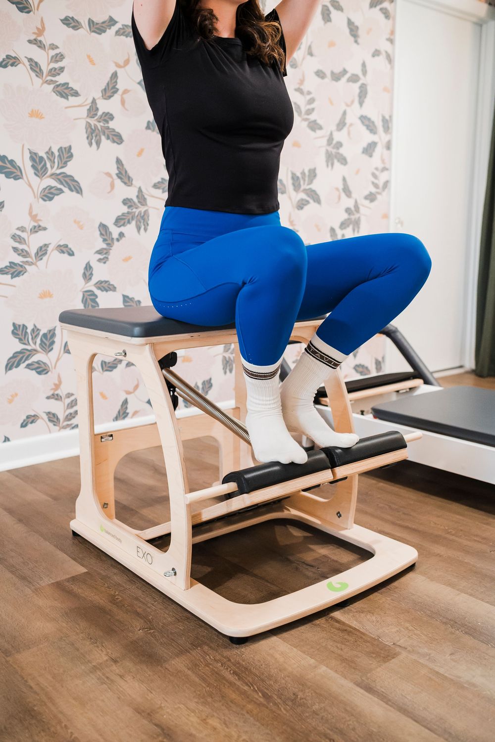 Person demonstrating proper form on a specialized exercise machine wearing blue leggings and black top.