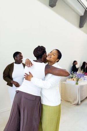 Two people embracing and dancing together in formal attire against a white wall.