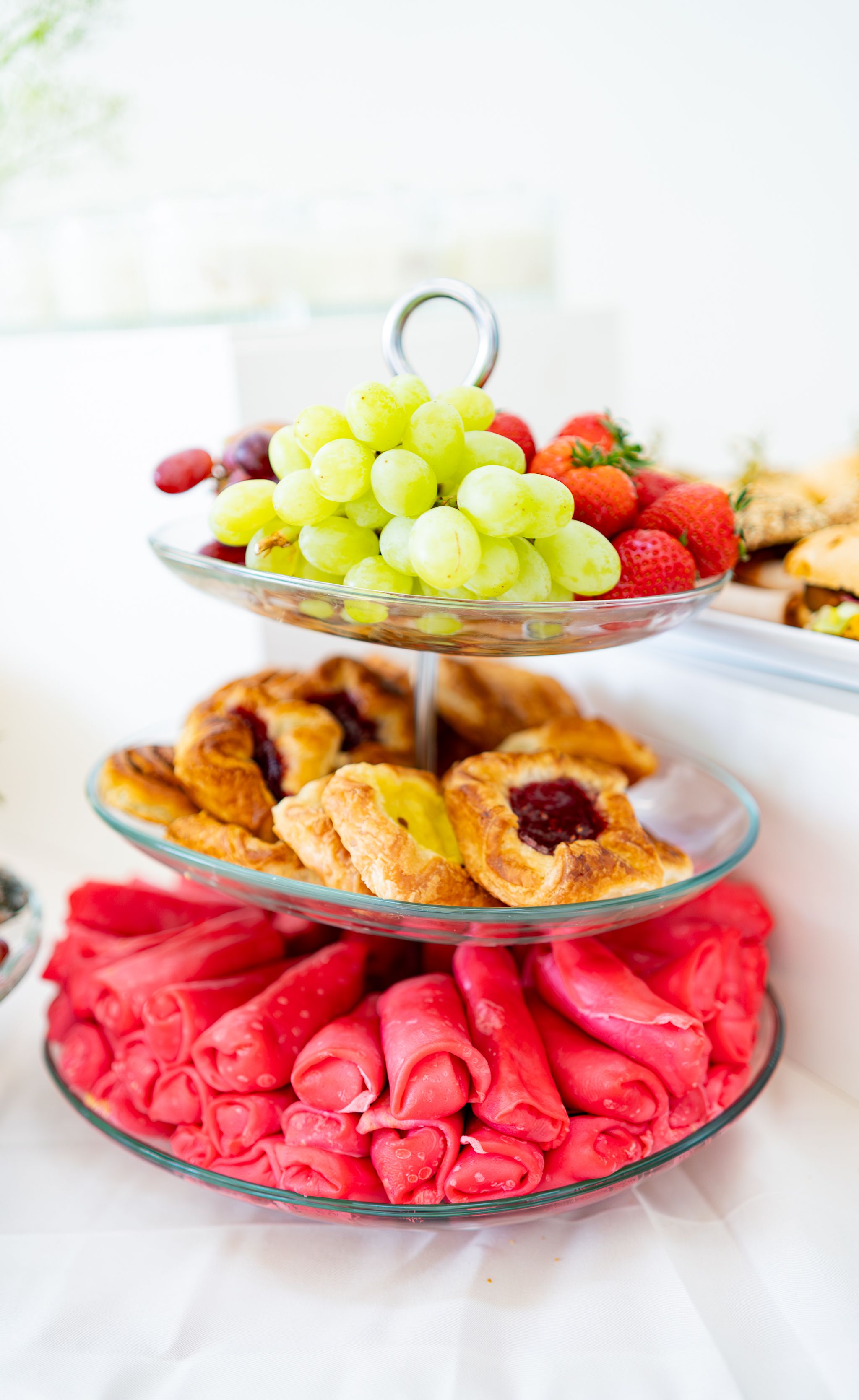 A three-tiered serving stand displays fresh fruit and pastries with red napkin decorations.