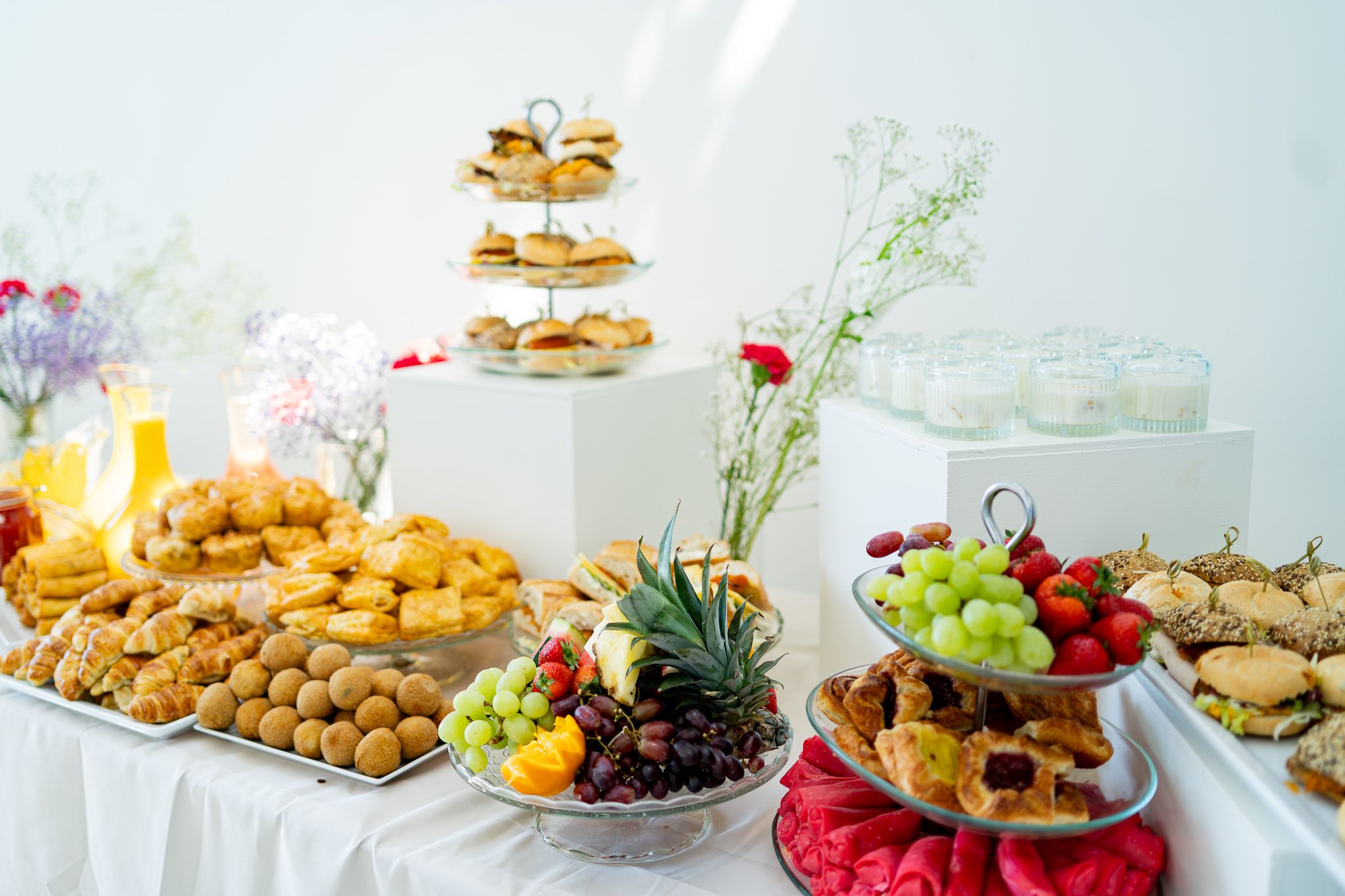 An elegant buffet spread features pastries, fruits and tiered serving platters on a white tablecloth.