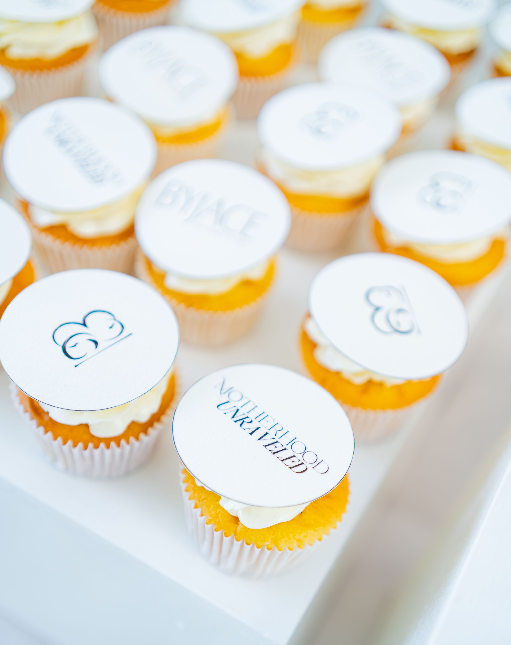 Rows of elegant cupcakes with white frosting and delicate decorative details arranged on a display.