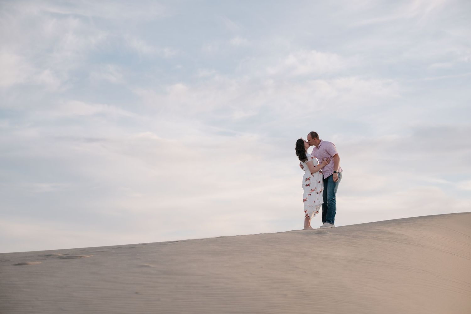 Couple embracing on sand dunes for a maternity shoot. Des Moines wedding photographer Holly Owens ready for your authentic session inquiry.