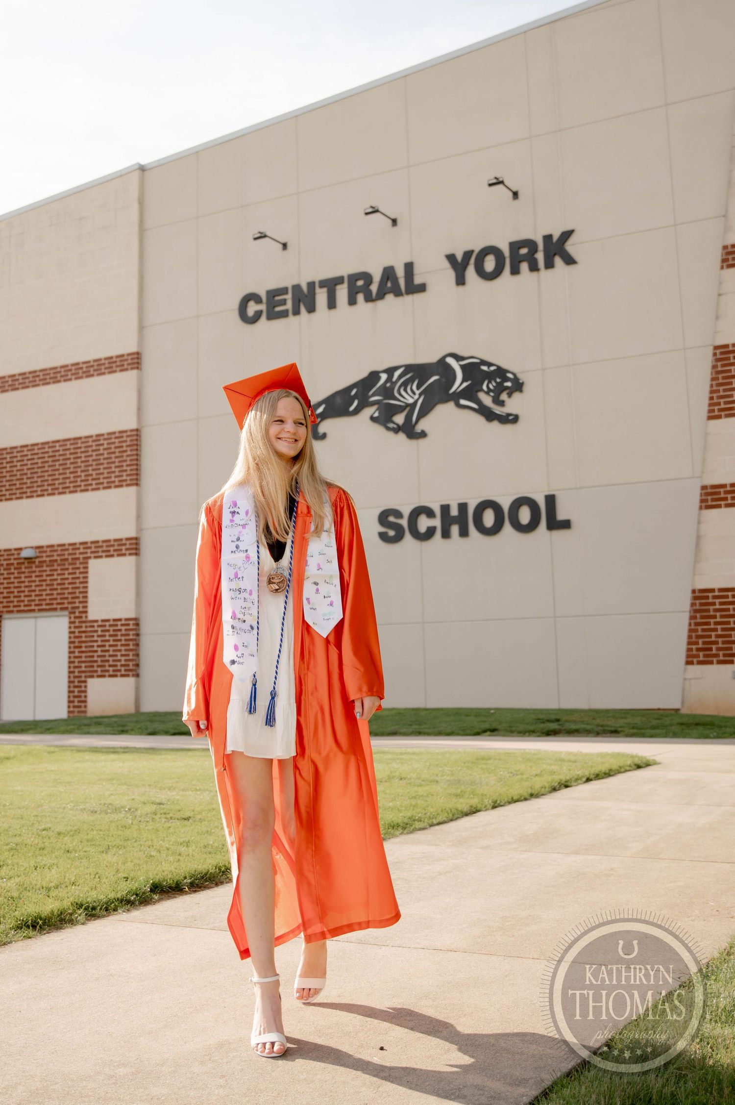 A graduation photo series showing someone in orange cap and gown in front of Central York School exterior wall.