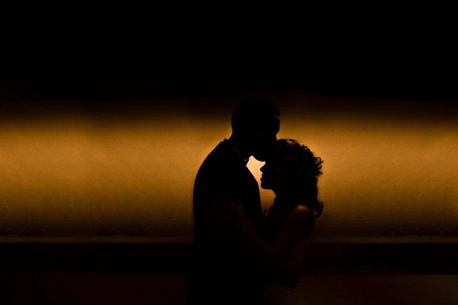 Silhouette of a romantic couple against a warm glowing orange background at sunset.