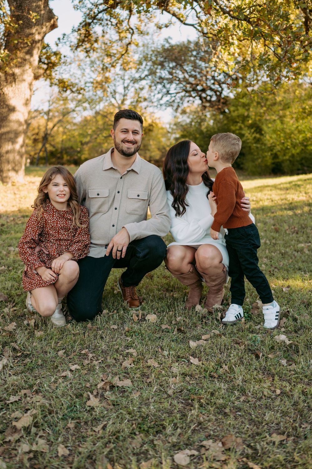 A family poses together on grassy hill during golden hour with autumn trees in background.