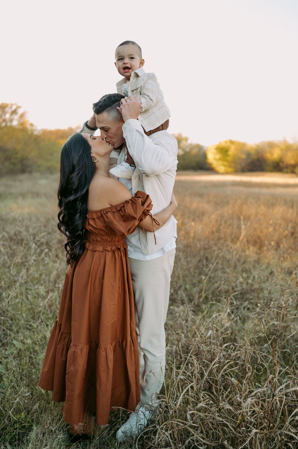 A family shares a tender moment together in a sunlit field at golden hour wearing earth-toned clothing.