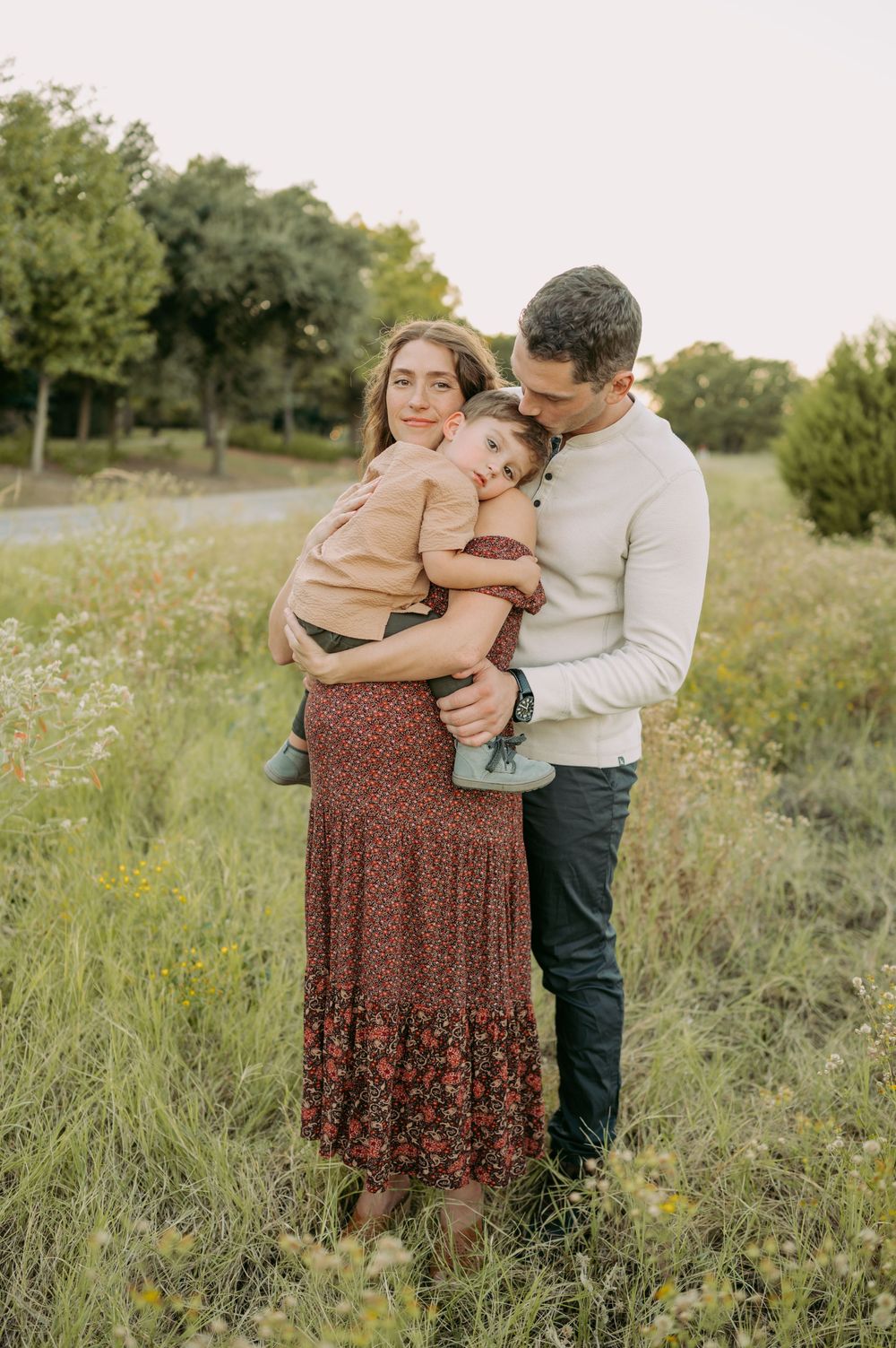 A family embraces tenderly in a meadow filled with wildflowers at sunset.