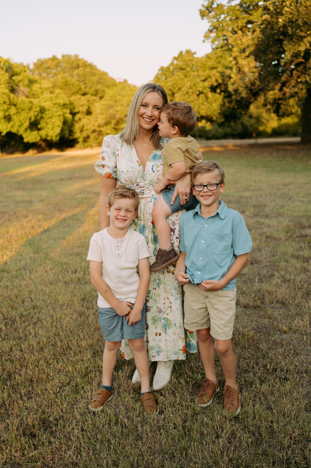 A family poses together on a grassy field during golden hour with autumn trees in the background.