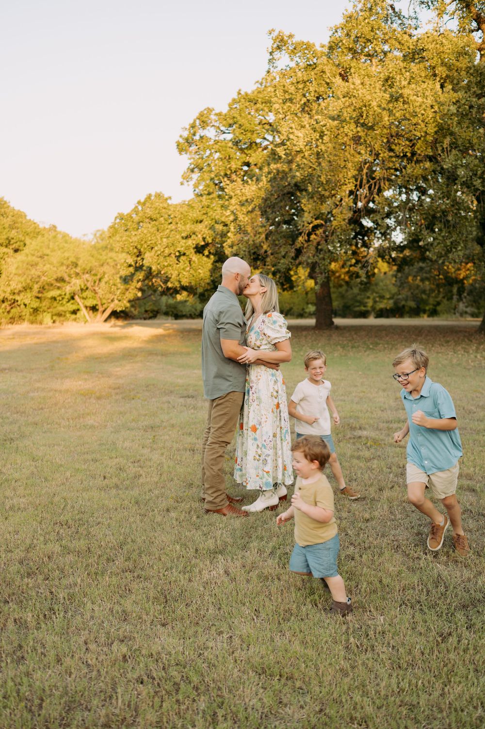 A group shares a tender moment in a sun-drenched field at golden hour with autumn trees in the background.