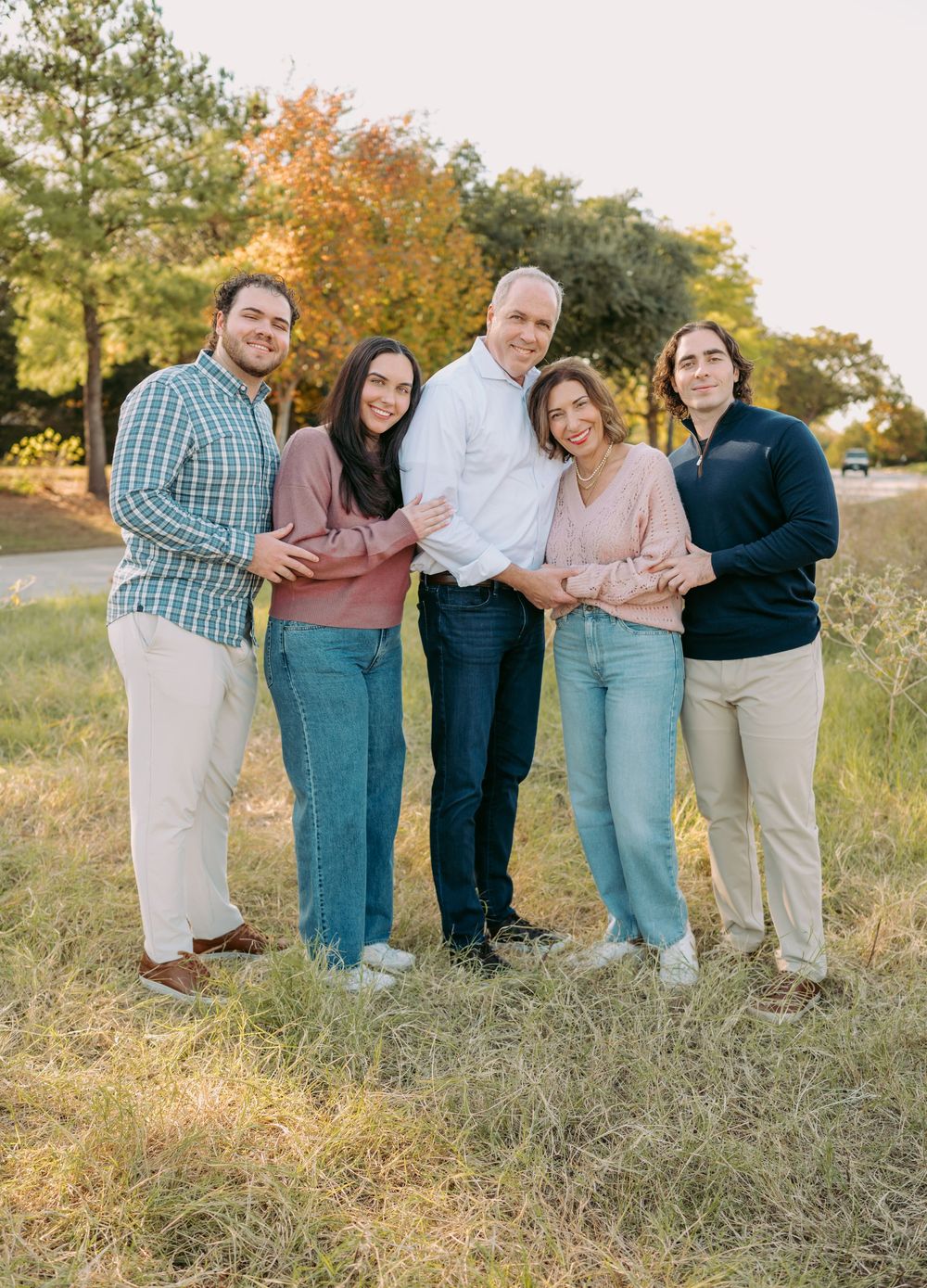 A multigenerational group enjoys a warm autumn day outdoors in casual attire, posing together on grassy terrain.