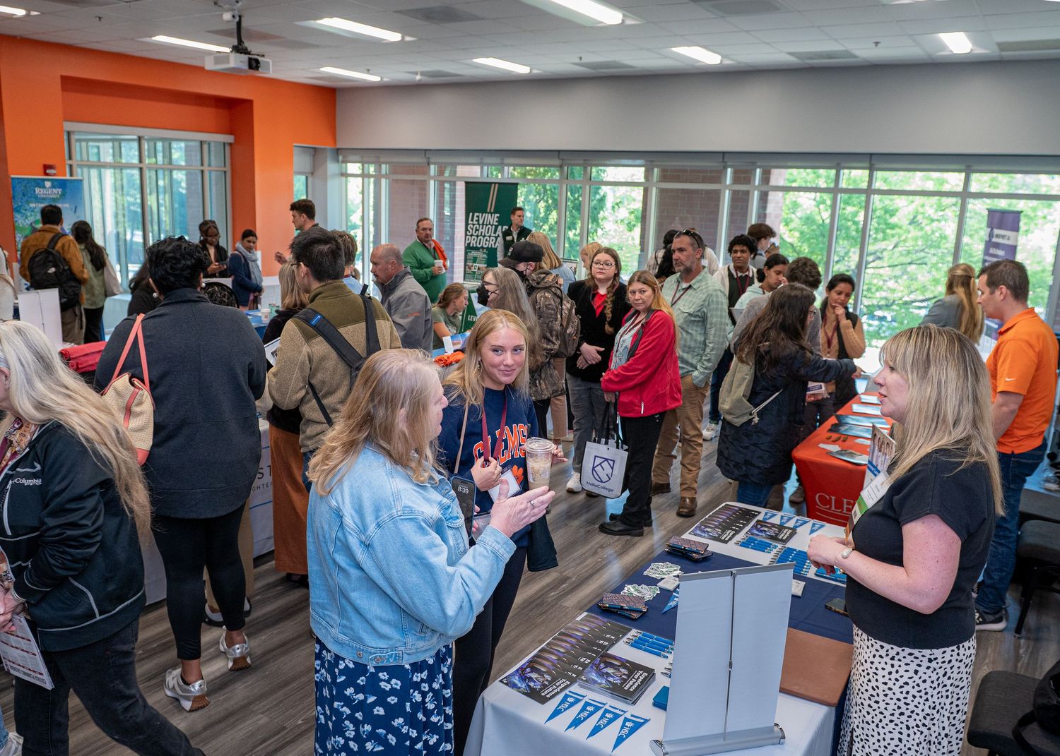Busy college fair with multiple information booths and visitors browsing materials.