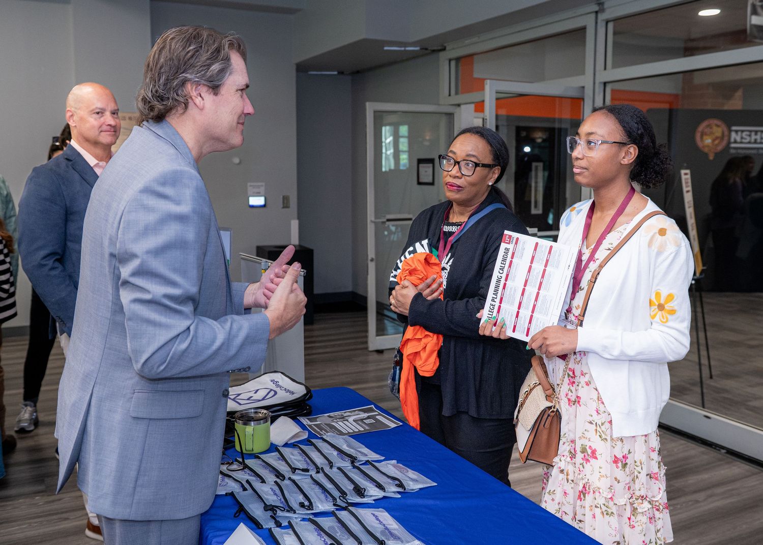 Educational fair with representatives staffing tables and engaging with attendees.