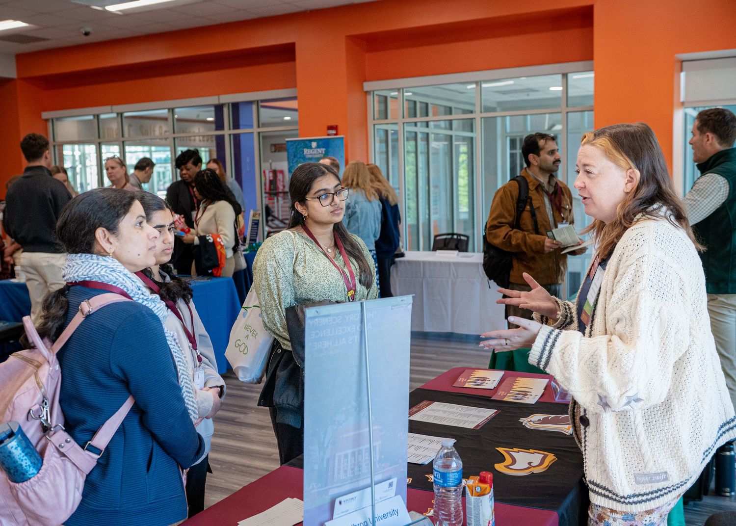 University event space with orange walls showing multiple information stands and attendees.